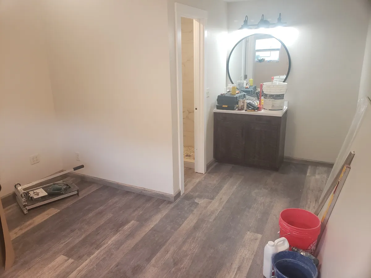 Bathroom remodel with dark vanity, round mirror, and LVP wood-look flooring